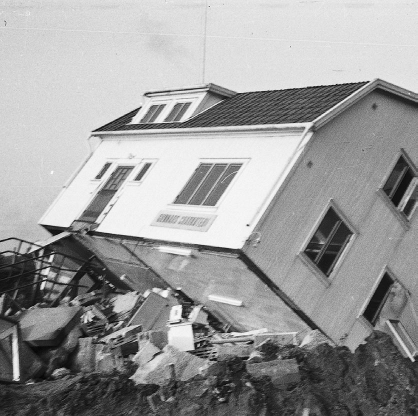 House tilted precariously on a slope with debris