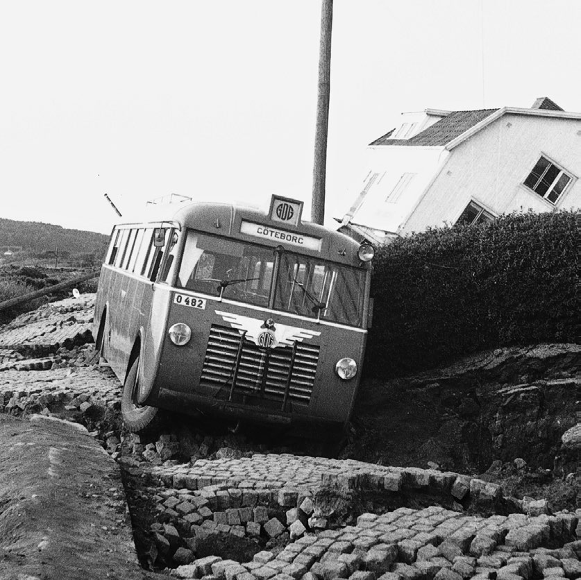 Old bus stuck in a large hole with a damaged building behind