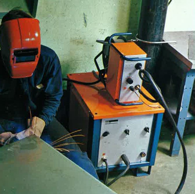 Worker welding with the AGA MIG 300 — sparks visible, red welding helmet